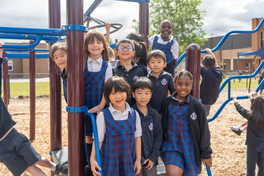Smiling diverse elementary schoolchildren pose together on a colorful playground, wearing school uniforms in bright outdoor light.